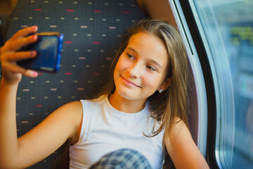 Little smiling girl travels by train while communicating via video conference on phone, takes...
