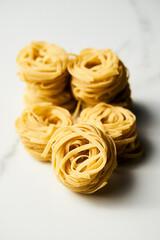 Dry tagliolini or tagliatelle pasta in nests in the bowl on white marble background. Uncooked ingredient