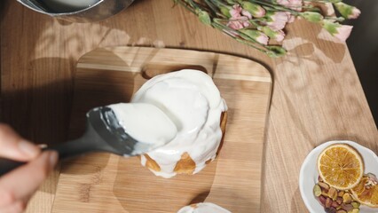 Top view a woman covers a homemade Easter cake with white icing.
