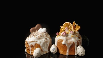 Two Homemade Easter Cakes Surrounded by Small Eggs on a Black Background.