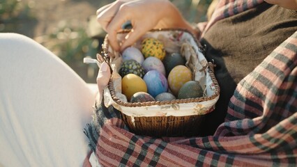 Close-up of a young woman who is sitting and holding a basket with Easter decorated eggs. Sunny.