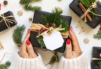 Hands with Christmas present with blank gift tag, with fir branches and decor, Mockup