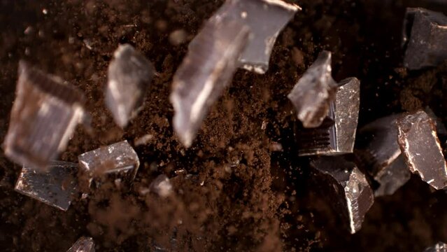 Super slow motion macro of raw bio organic dark bitter chocolate bar chunks are falling in cocoa powder at 1000 fps.