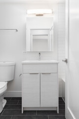 A bathroom detail with a white wood cabinet, dark grey tile floor, and a light mounted above the mirror.