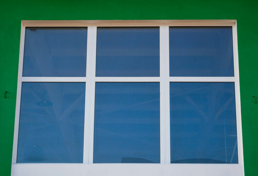 Big PVC window with insulated glass on green wall, reflecting blue sky.