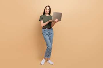 Full body photo of smiling happy young woman working freelancer doing easy tasks for money using laptop isolated on beige color background