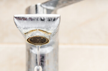 Water drop dripping from old limescale tap