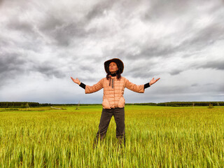 An adult girl looking like a cowboy in a hat in a field and with a stormy sky with clouds takes pictures of a rainbow and takes selfie in the rain. Woman having fun outdoors on rural and rustic nature