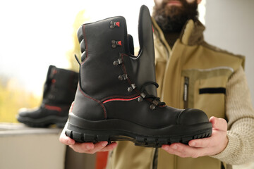black work boots made of leather with reinforced cape, high top in hands of young bearded man,...