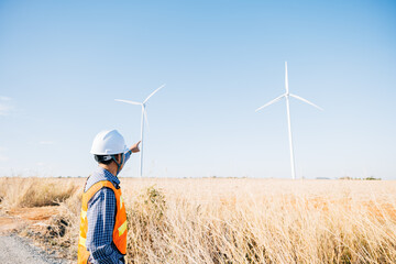 Engineer in helmet inspects windmill farm for clean energy. Asian technician ensures turbine...