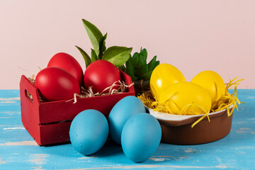Easter eggs of different colors in a basket and pots with straw