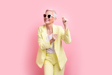 Portrait photo of cheerful mature businesswoman shopaholic wear yellow suit dancing at friday party isolated on pink color background