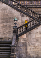 Stylish elegant woman in a yellow coat on the steps. Happy female traveler looking at tourist...