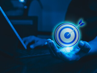 Businessman hand holding big goal, target dart icon while working with laptop computer, blue tone....