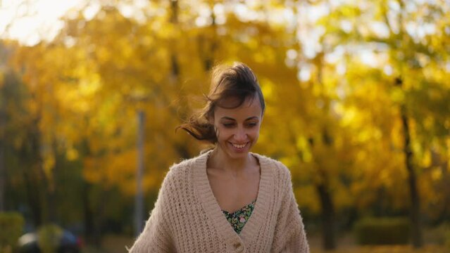 stunning young brunette woman in autumn forest with yellow foliage against sunset sun with sunflare. stylish attractive girl walks in park at warm fall day. slow motion 4k footage