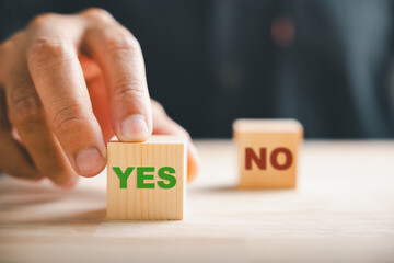 Hand of businessman selects between two wooden cubes marking check for right and wrong choices....