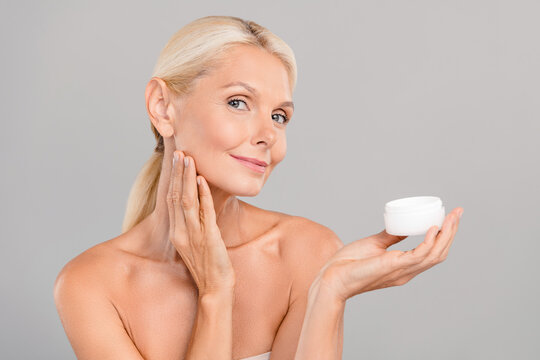 Photo of positive cute senior lady nude shoulders applying cheekbone face cream empty space isolated grey color background