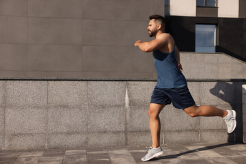 Naklejka premium Young man running near building outdoors. Space for text
