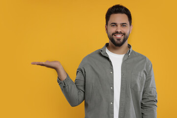 Special promotion. Smiling man holding something on orange background. Space for text