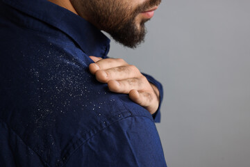 Man brushing dandruff off his shirt on grey background, closeup. Space for text