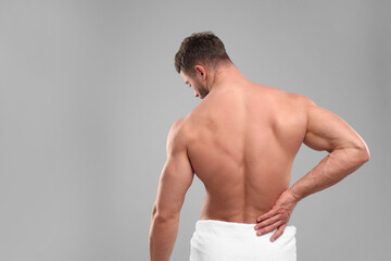 Man suffering from back pain on grey background, back view. Space for text