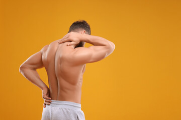 Man suffering from back and neck pain on orange background, space for text