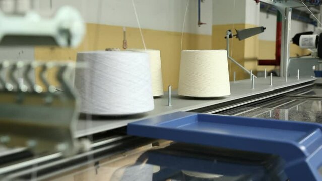 The knitting machine uses threads from bobbins mounted on top. A row of industrial textil flat knitting machines in a knitwear factory. Manufacture of knitwear, modern computerized flat Knitting