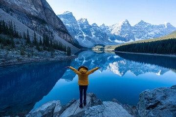 Female tourist carries a backpack, travels, walks, climbs, sits and admires the beauty of the reflection in the water of moraine Lake, Canadian Rocky Mountains