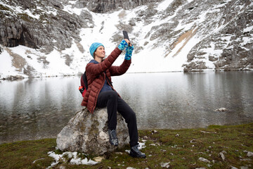 Smiling Woman Hiker Taking a Selfie Sitting on a Rock of High Mountain Alpine Lake
