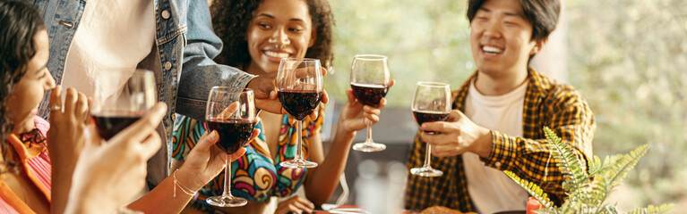 Group of happy young friends is drinking wine while having holiday dinner home party together - obrazy, fototapety, plakaty