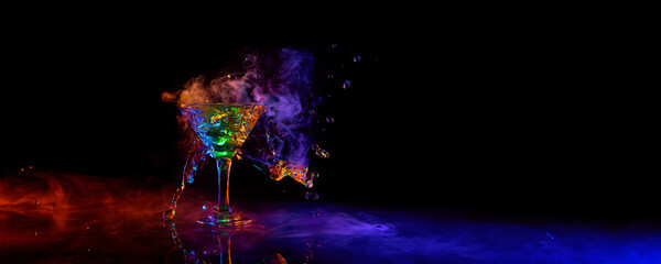 Glass of martini cocktail standing against dark background with neon light with smoke. Splashes....