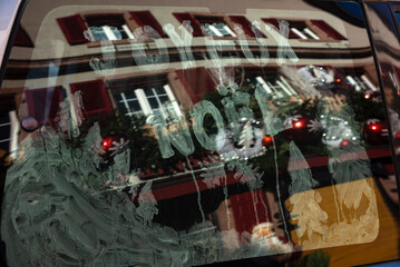 Alsace, France. Christmas "Joyeux Noel" greeting ("Merry Christmas" in French) and snowy forest decoration on car window. Reflection of festive decorated street. Winter holidays celebration and travel