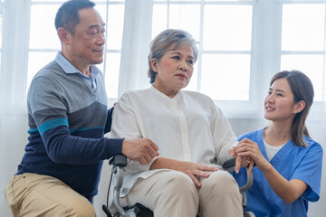 Fototapeta premium Asian young nurse support couple senior older man and woman in a wheelchair. elderly mature and a group of senior friends living in the hospital. socializing of retired people.