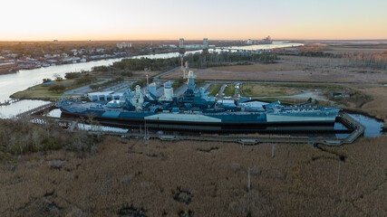 Battleship at sunrise in Wilmington, North Carolina, with the Cape Fear River flowing on the left and the Cape Fear Memorial Bridge in the distance, set against a backdrop of the awakening city.