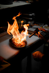 Chef frying sushi rolls in an oval shape using a gas burner