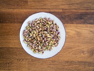 Peeled bare naked pistachio nuts on a white plate on a wooden table