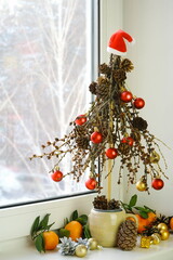 Traditional decorations for the New Year holiday. Mini Christmas tree   handmade from branches and pine cones decorated red and gold balls. Alternative Christmas decor on the windowsill.