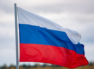 The white-blue-red flag of the Russian Federation is flying in the wind against a cloudy sky.
