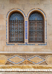 Mamluk archirtecture style pair of arched windows framed by a rustic brick wall. The intricate...