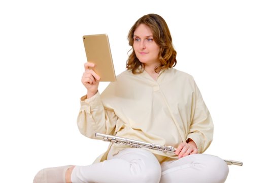 Happy woman musician with flute looks into tablet at home on sofa in living room, isolated on a white background