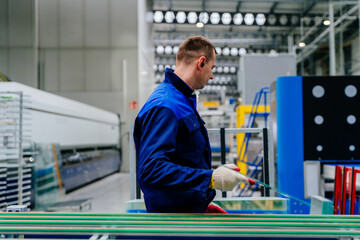 A man worker monitoring quality and controls the operation of a machine at a glass cutting factory. Adult man working in glass processing factory, stacking cut glass.