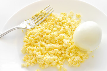 Mashed boiled egg with a fork on a white plate. Egg sandwich cooking preparation concept.