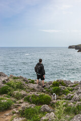 Back view of a mature man with backpack looking at the sea with his dog in nature. Travel and nature concept