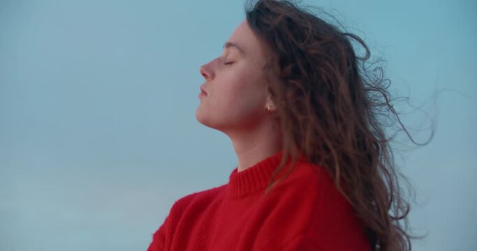 Cinematic portrait of young pensive woman breathe in fresh ocean breeze air, wind blow her hair around. Holistic and self love lifestyle. At peace with oneself. Self search and inner world