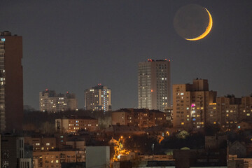 The narrow crescent of the setting young moon over the city skyline, Kyiv, Ukraine.