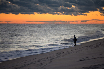 Fisherman silhouette on the beach surfcasting during sunset. Robert Moses State Park, Long Island, New York.