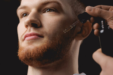 Young man holding pipette with oil for beard hair. Concept spa cosmetic and treatment wellness and...