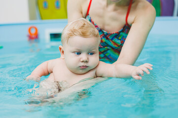 Fototapeta na wymiar A baby learns to swim in a pool with a trainer. Baby learning to swim. Child development.