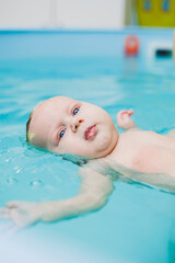 Teaching children to swim. A baby learns to swim in a pool with a trainer. Baby learning to swim. Child development.