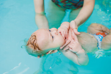 Teaching children to swim. A baby learns to swim in a pool with a trainer. Baby learning to swim. Child development. - obrazy, fototapety, plakaty